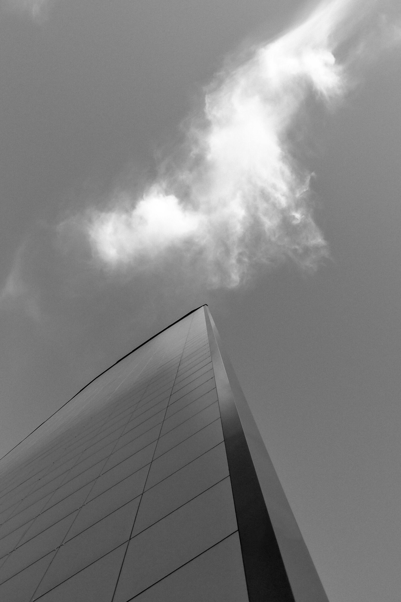 Grayscale image of a modern skyscraper reaching towards the sky with clouds.